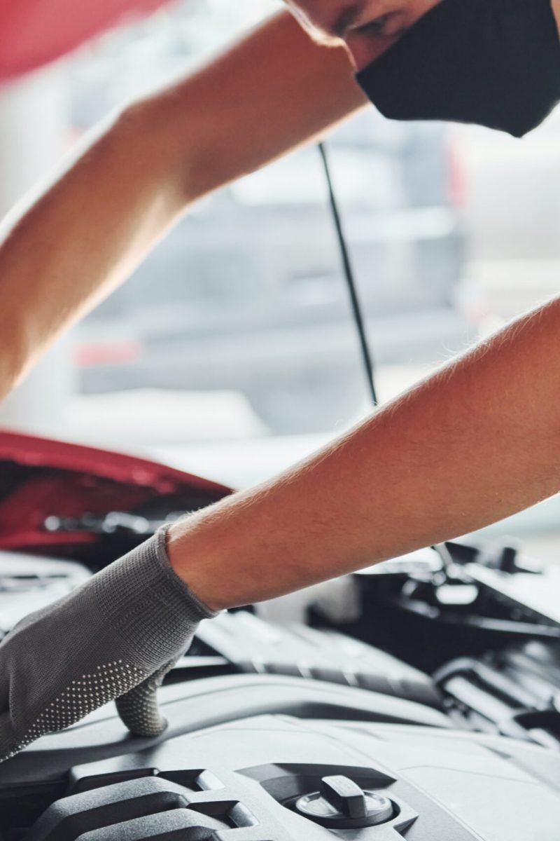 Man in uniform works with broken automobile. Conception of car service.