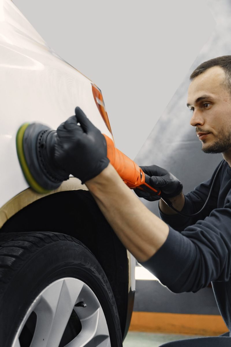 Man in a garage. Worker polish a car. Man in a black uniform.