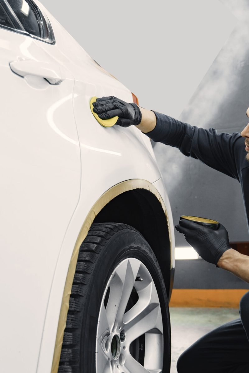 Man polish a car in a garage Man in a garage. Worker polish a car. Man in a black uniform.